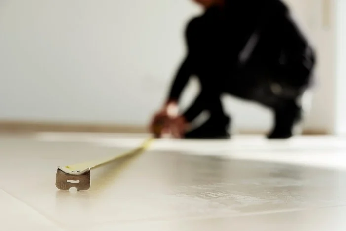 Person misst einen Boden mit Zollstock aus